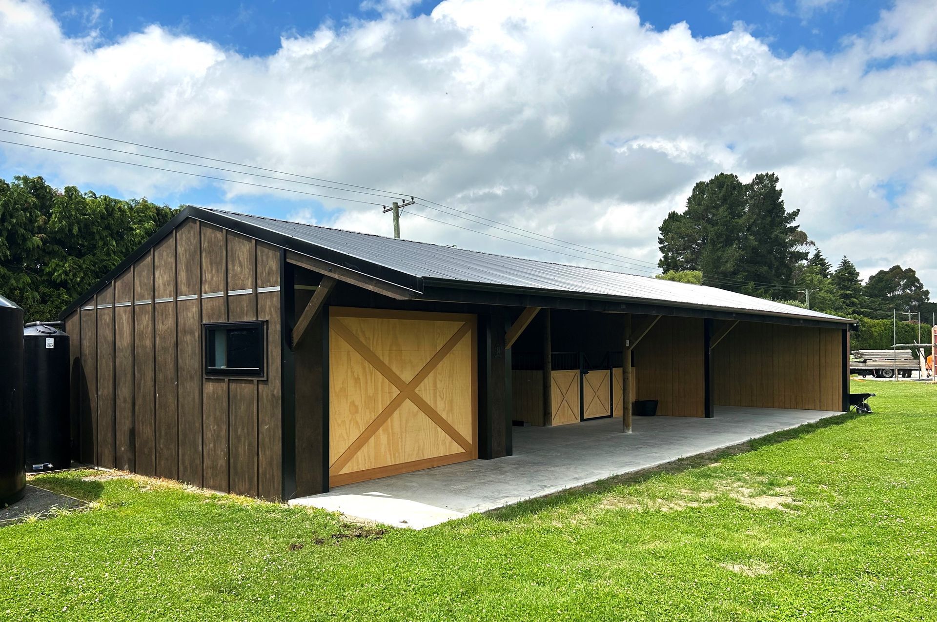 A large wooden barn is sitting in the middle of a lush green field.