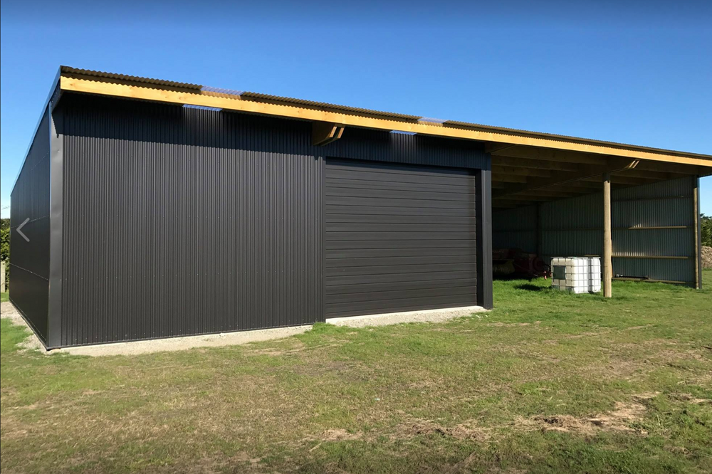 A large black building with a wooden roof is sitting in the middle of a grassy field.