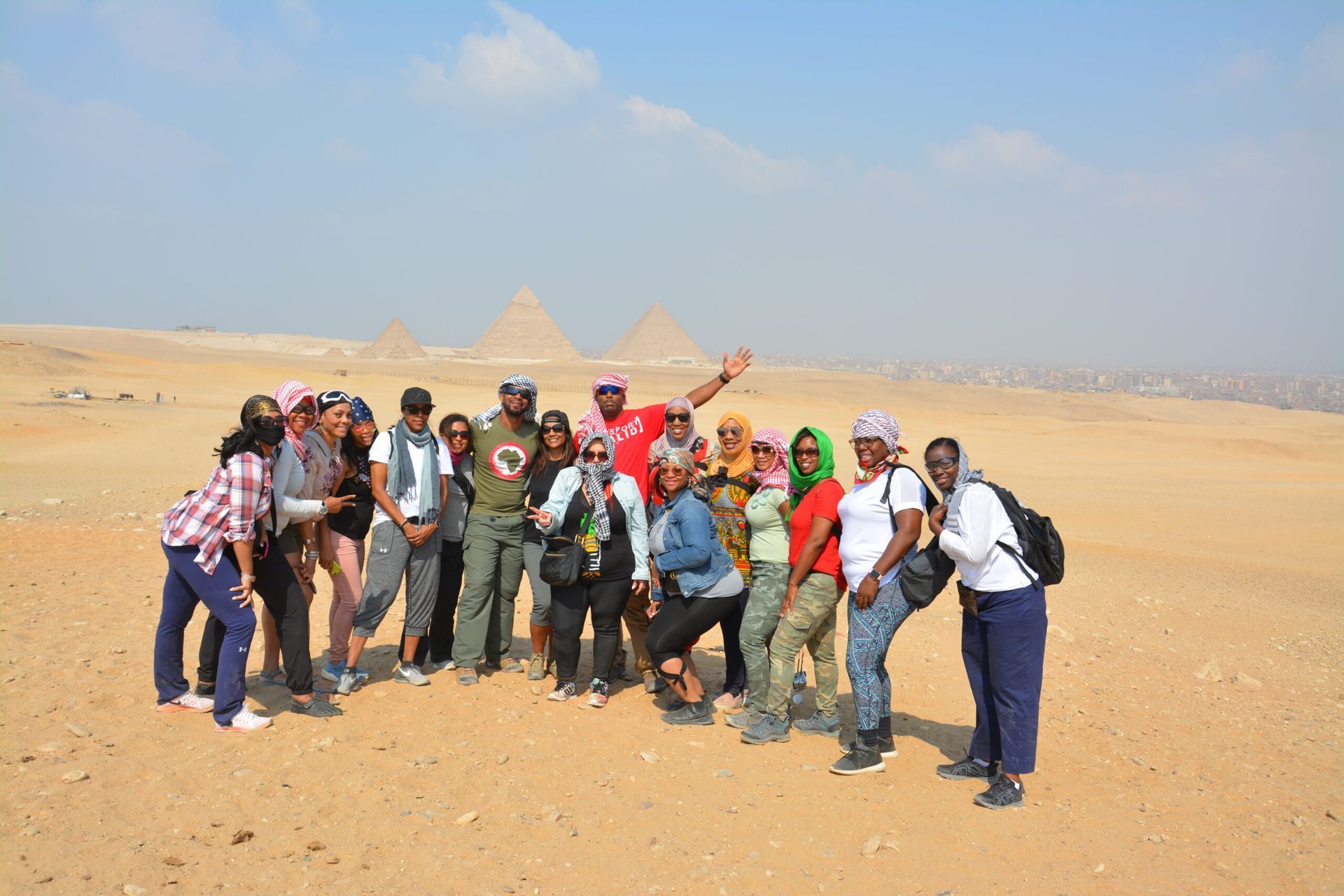 Group of hikers posing on desert sand with pyramids in the background under a clear blue sky