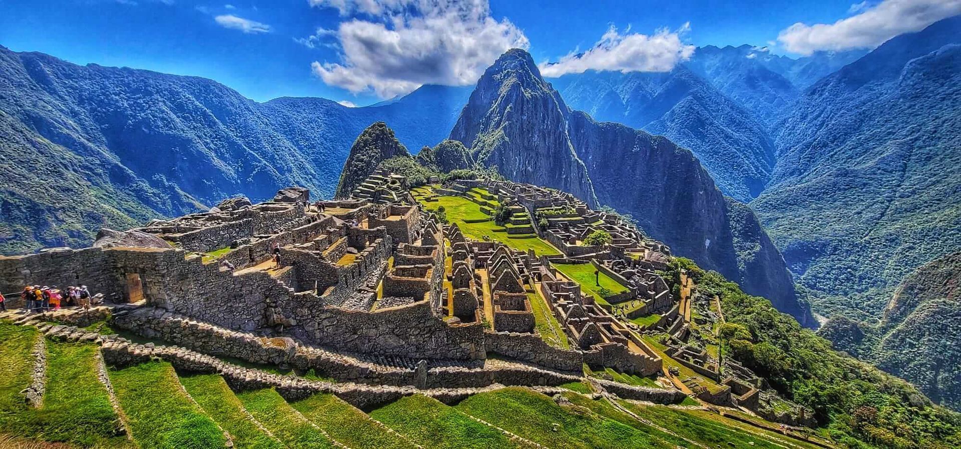 Machu Picchu ruins on a green mountain ridge under a bright blue sky with clouds