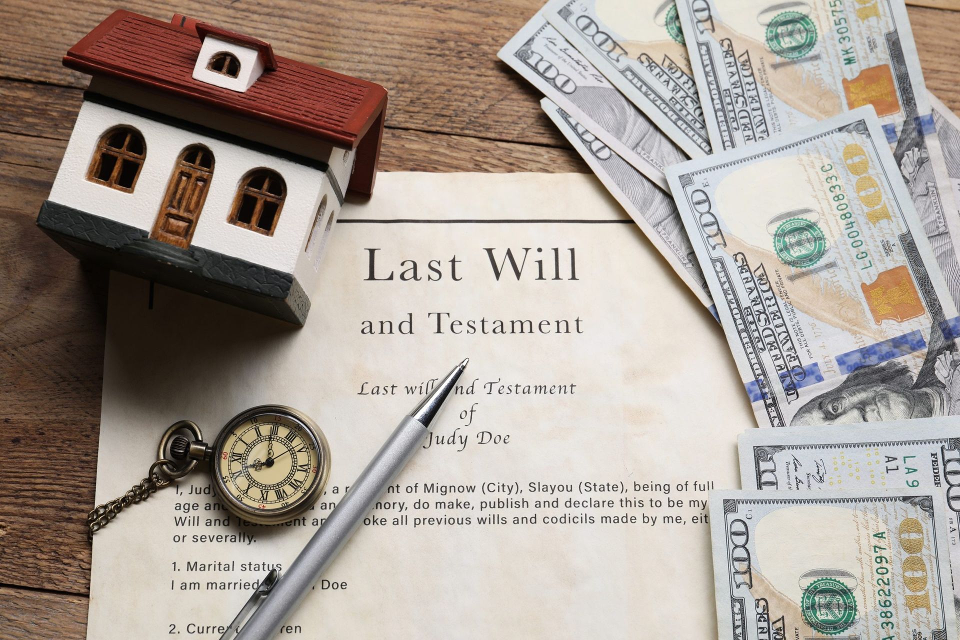 Last Will and Testament with model house, money, pen, and pocket watch on a desk