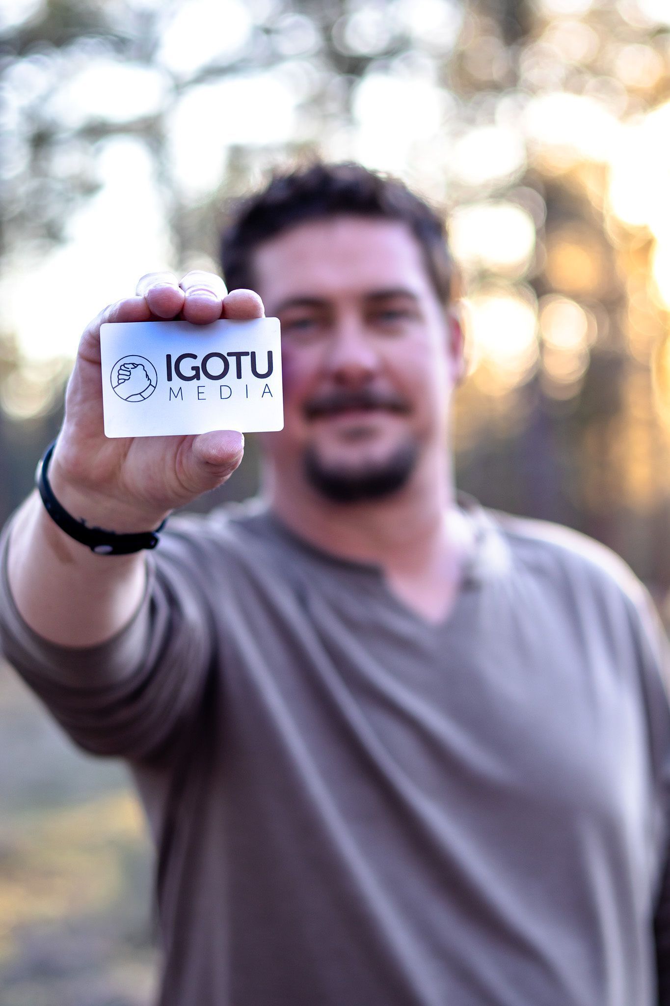Man holding up a small white card with black text outdoors, with a blurred sunny background