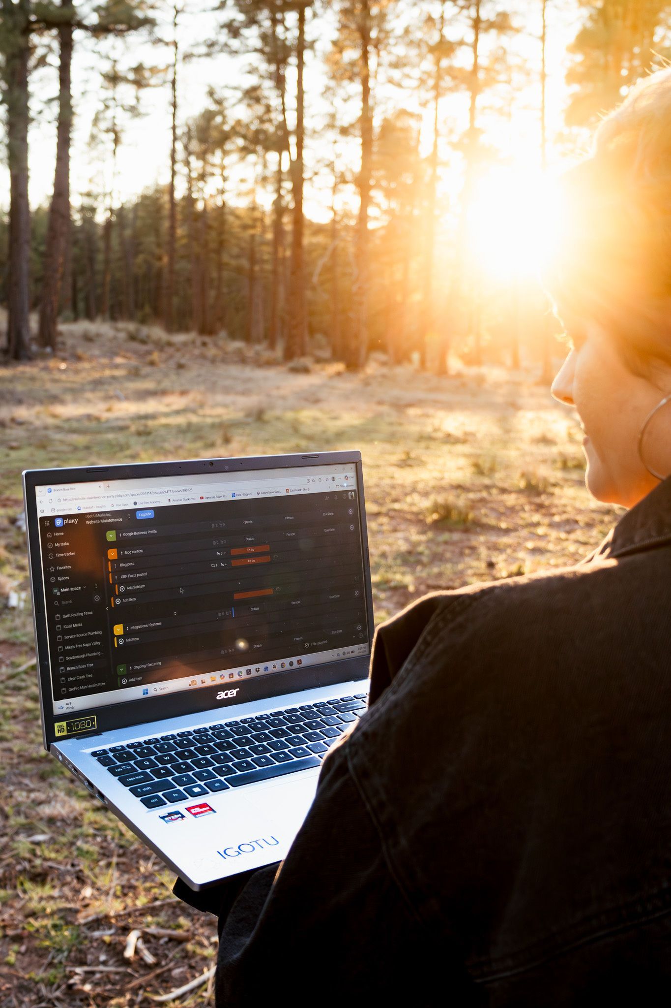 Person using a laptop outdoors in a sunlit forest at sunrise