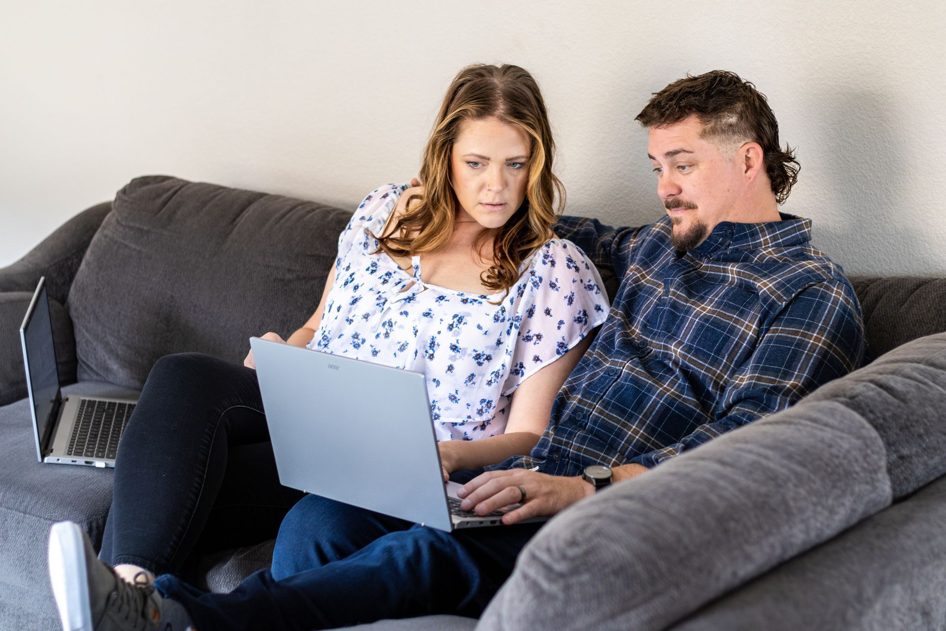 Two people on a gray couch looking at a laptop together
