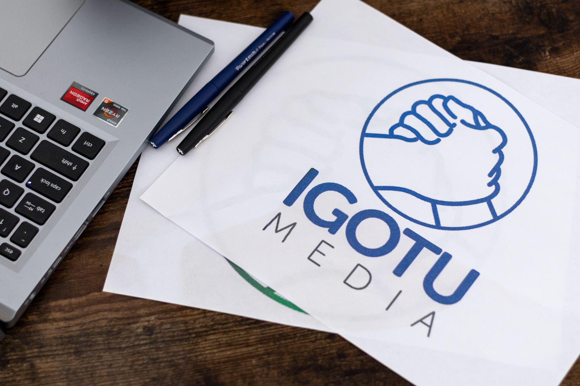 Laptop and pens on a wooden surface next to a paper featuring the blue 