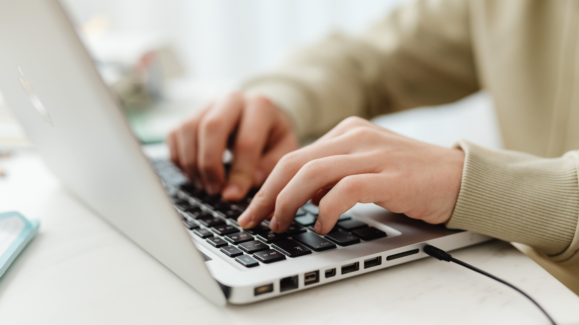 Hands typing on a laptop keyboard in a bright workspace