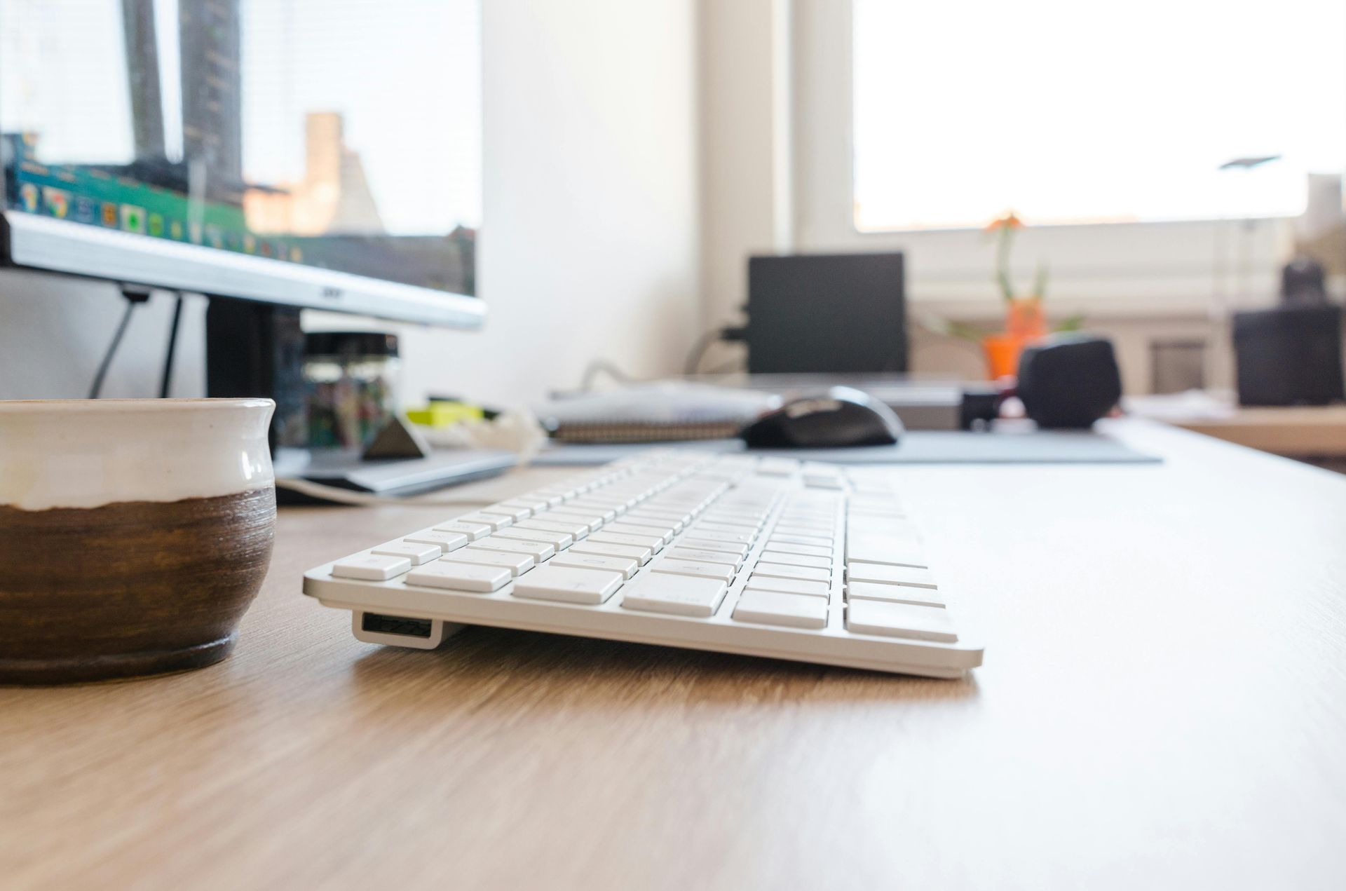 Desk with white keyboard, coffee cup, and computer monitors in a bright office workspace
