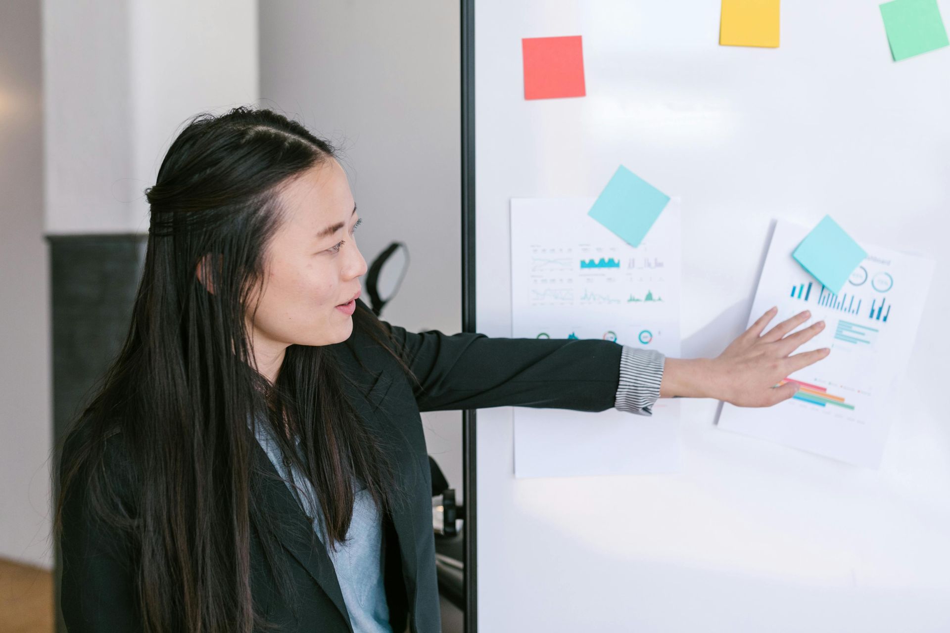 Woman pointing at notes on a whiteboard with colored sticky notes in an office setting