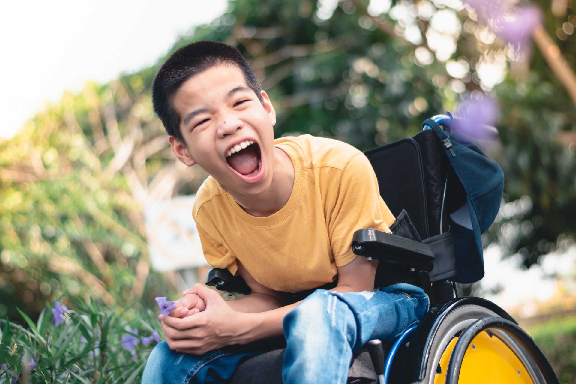 Smiling person in a yellow shirt sitting in a wheelchair outdoors in a green park Smiling person in a yellow shirt sitting in a wheelchair outdoors in a green park