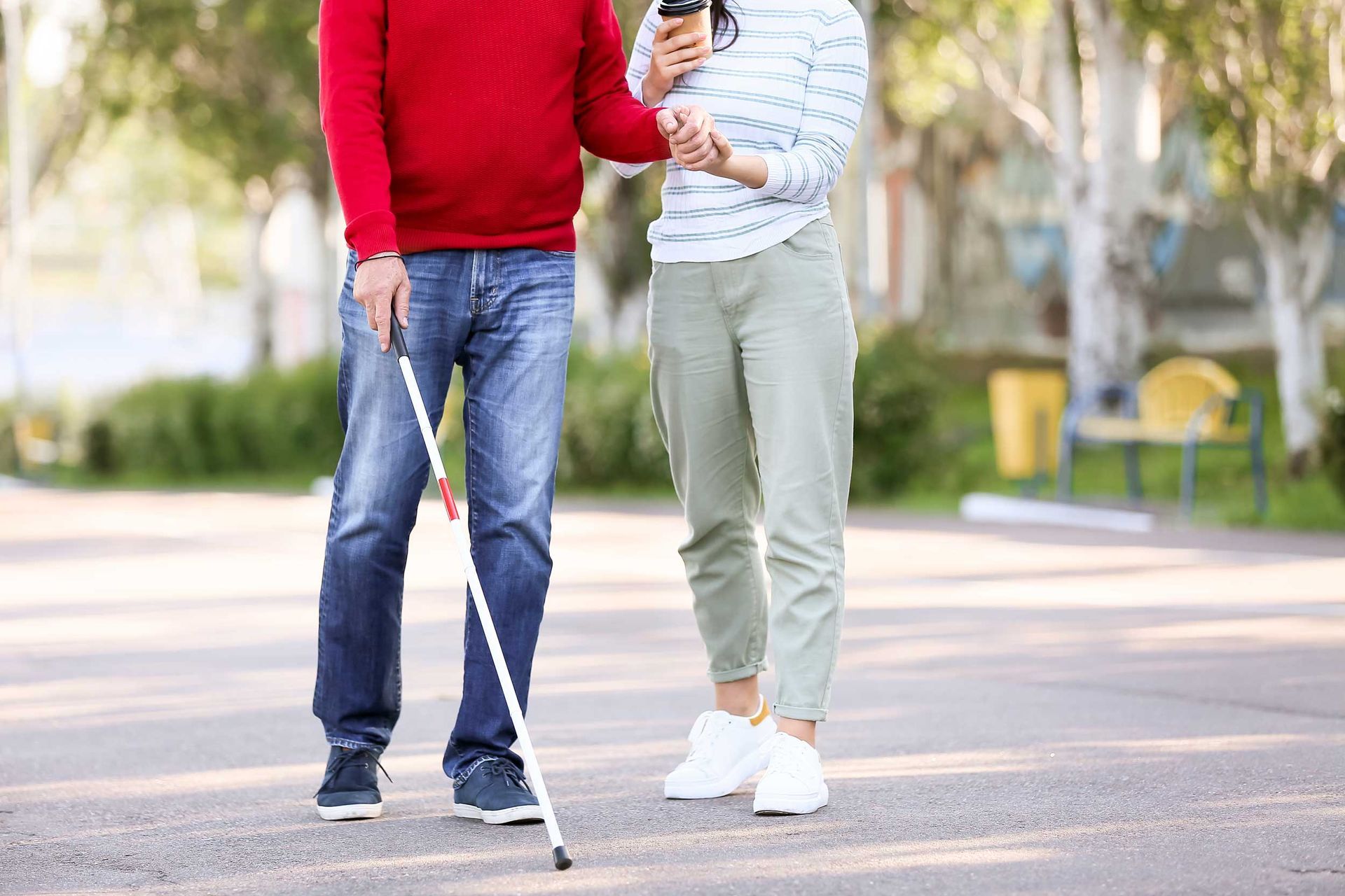 A blind man with a carer walking outdoors with his straight cane. A blind man with a carer walking outdoors with his straight cane.