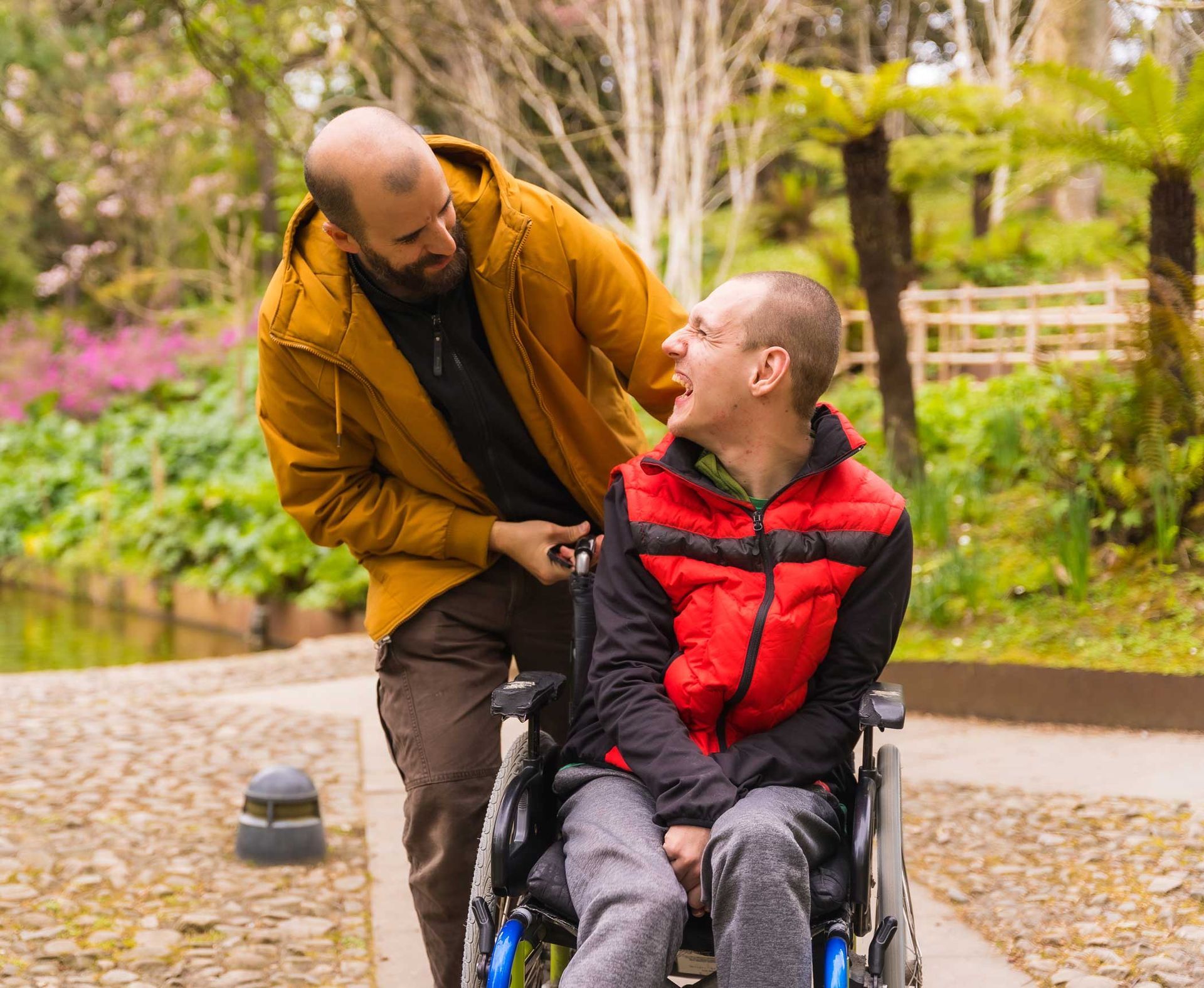 A person with a disability in a wheelchair laughing with a carer in a public park. A person with a disability in a wheelchair laughing with a carer in a public park.