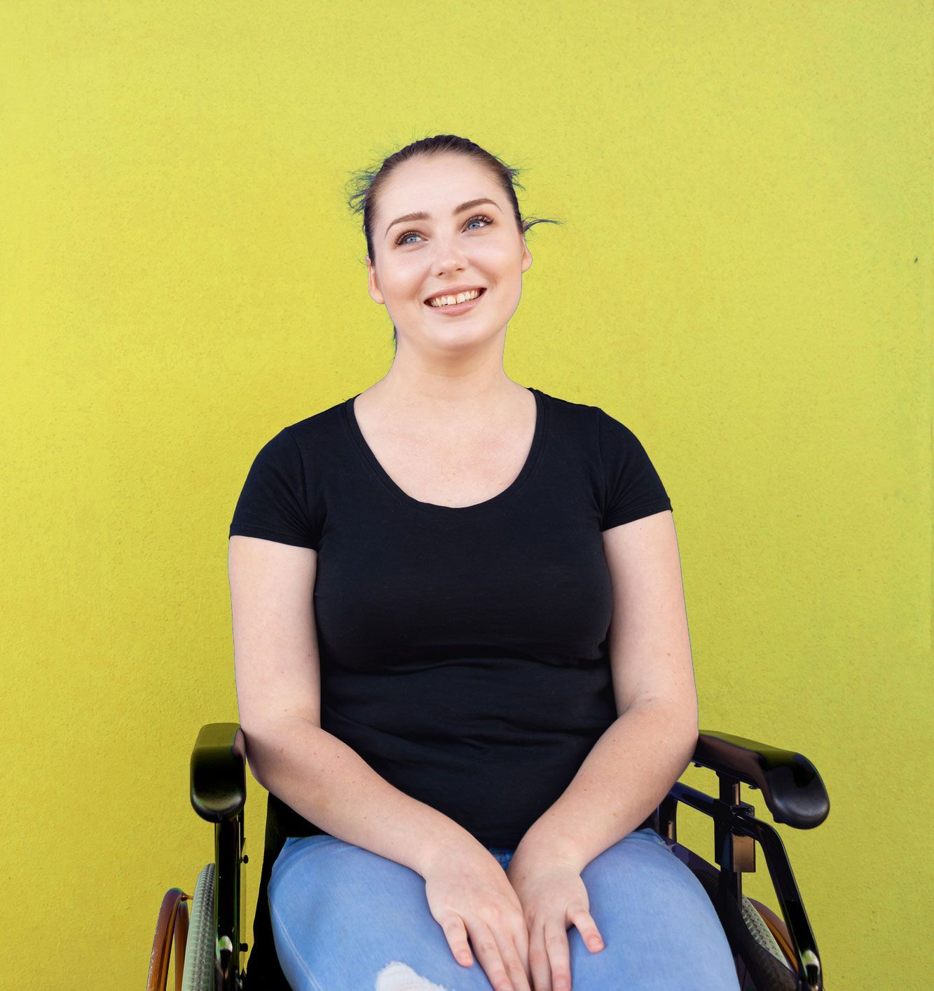 Woman in a wheelchair smiling against a yellow background, wearing a black shirt and jeans.