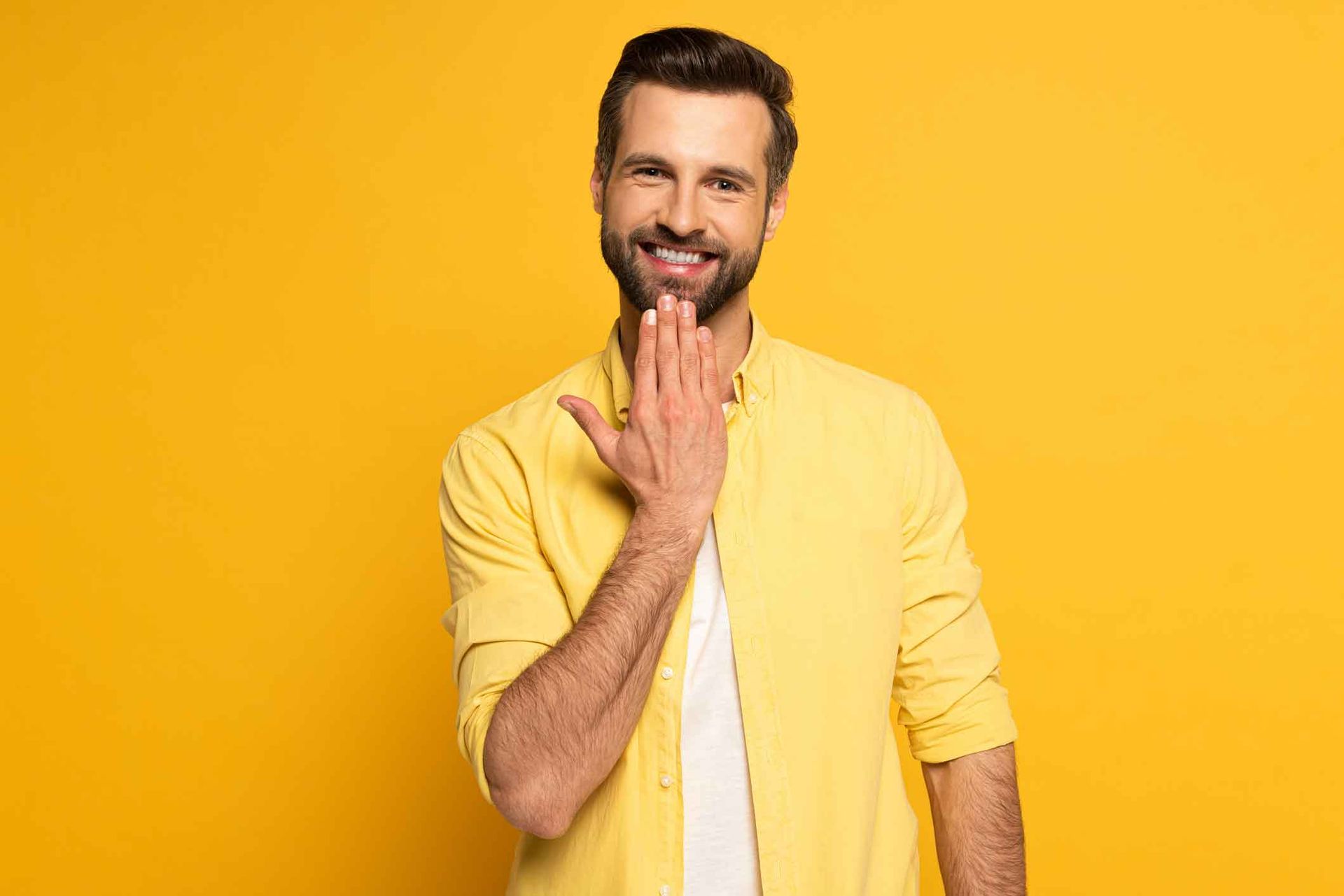 Man in yellow shirt smiles and gestures with his hand near his mouth against a yellow backdrop. Man in yellow shirt smiles and gestures with his hand near his mouth against a yellow backdrop.