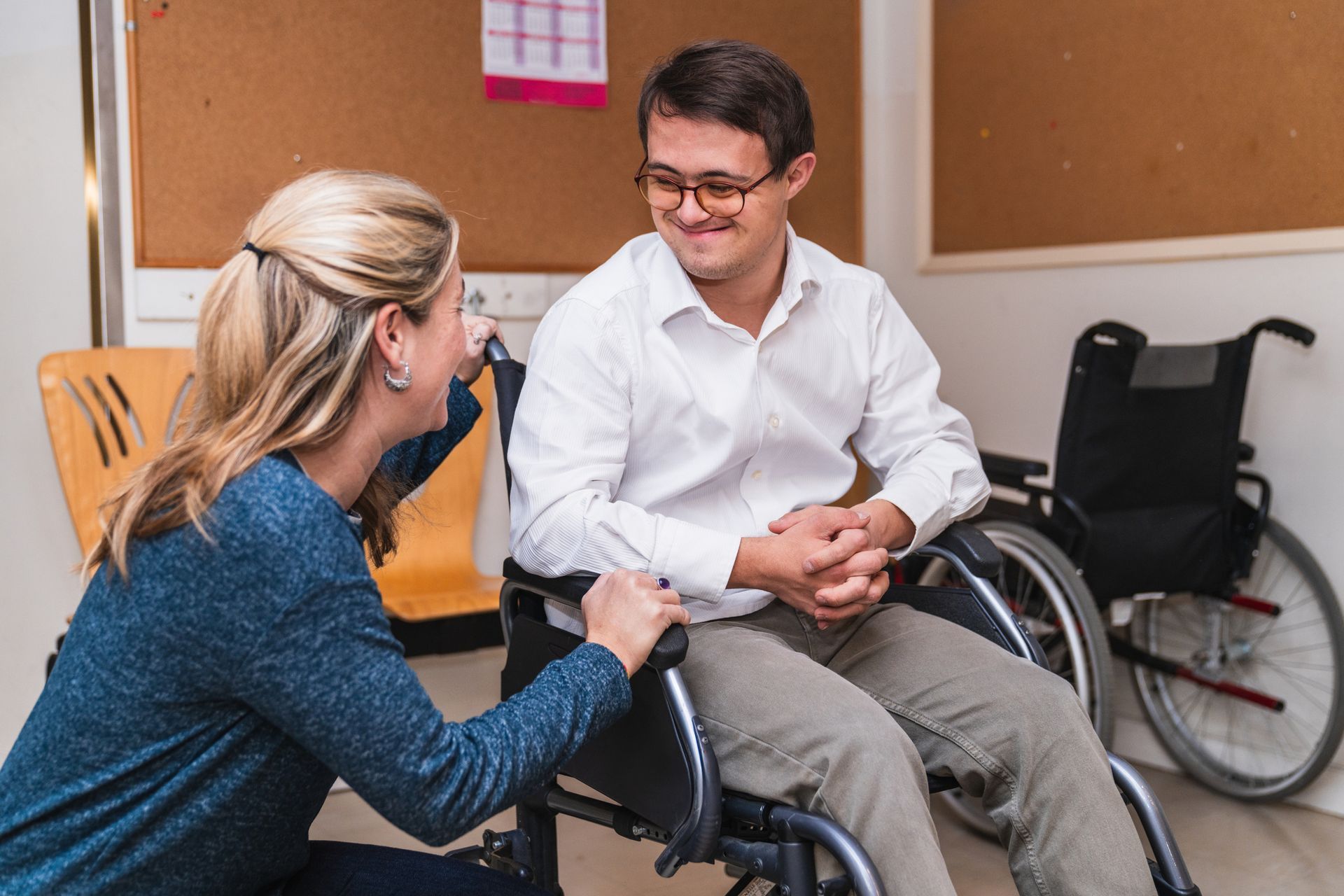 Female support worker speaks to a smiling man in a wheelchair. Female support worker speaks to a smiling man in a wheelchair.>