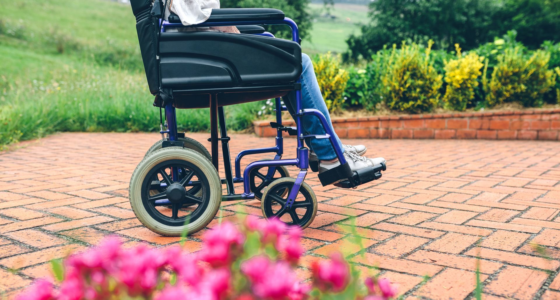 Person in wheelchair on brick path with flowers and greenery. Person in wheelchair on brick path with flowers and greenery.