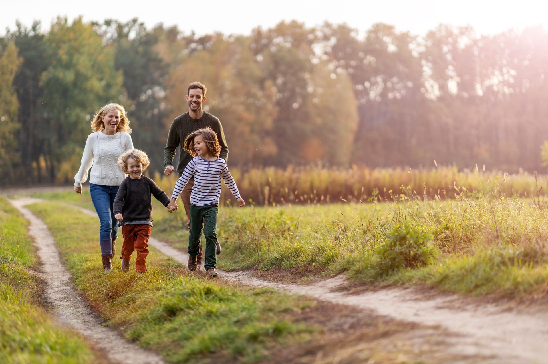 Family walking with two children on a dirt path beside a field at sunset