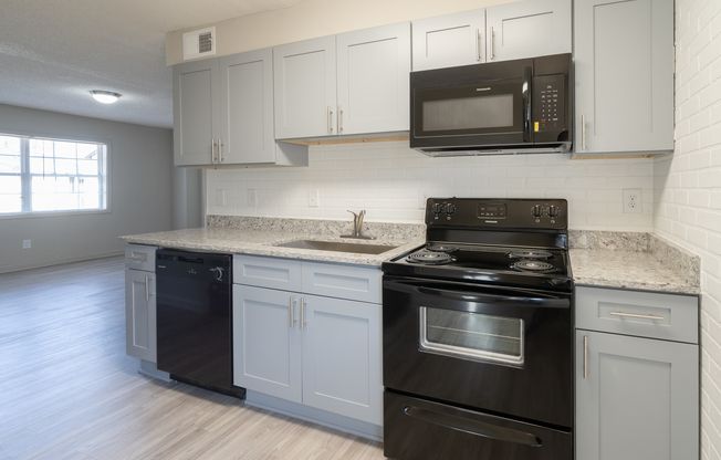 Bright white kitchen with black appliances, light cabinets, and a stainless sink and countertop.