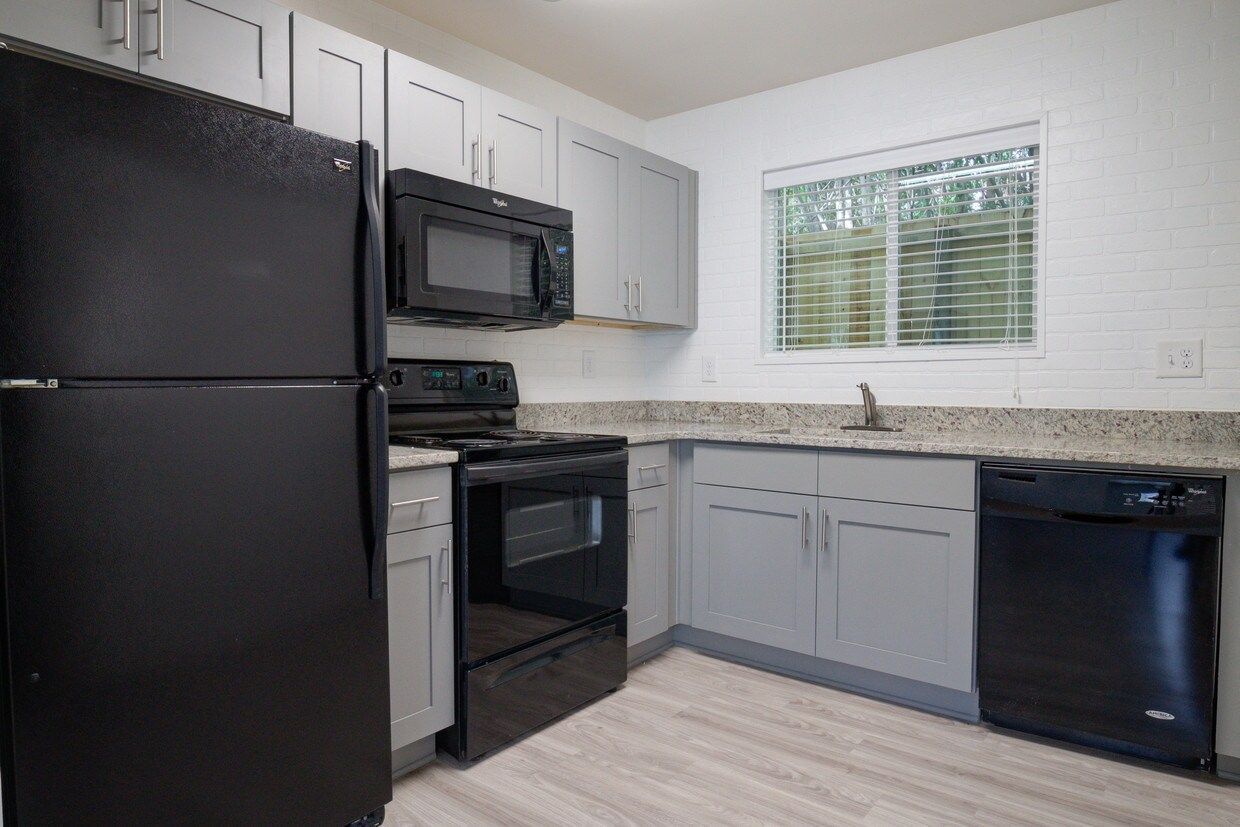Modern kitchen with black appliances, white cabinets, and gray lower cabinets by a window