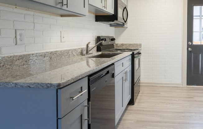 Modern kitchen with blue cabinets, granite countertop, stainless sink, and light wood flooring