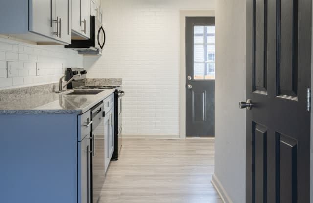 Modern kitchen hallway with white cabinets, blue lower cabinets, and a dark front door.
