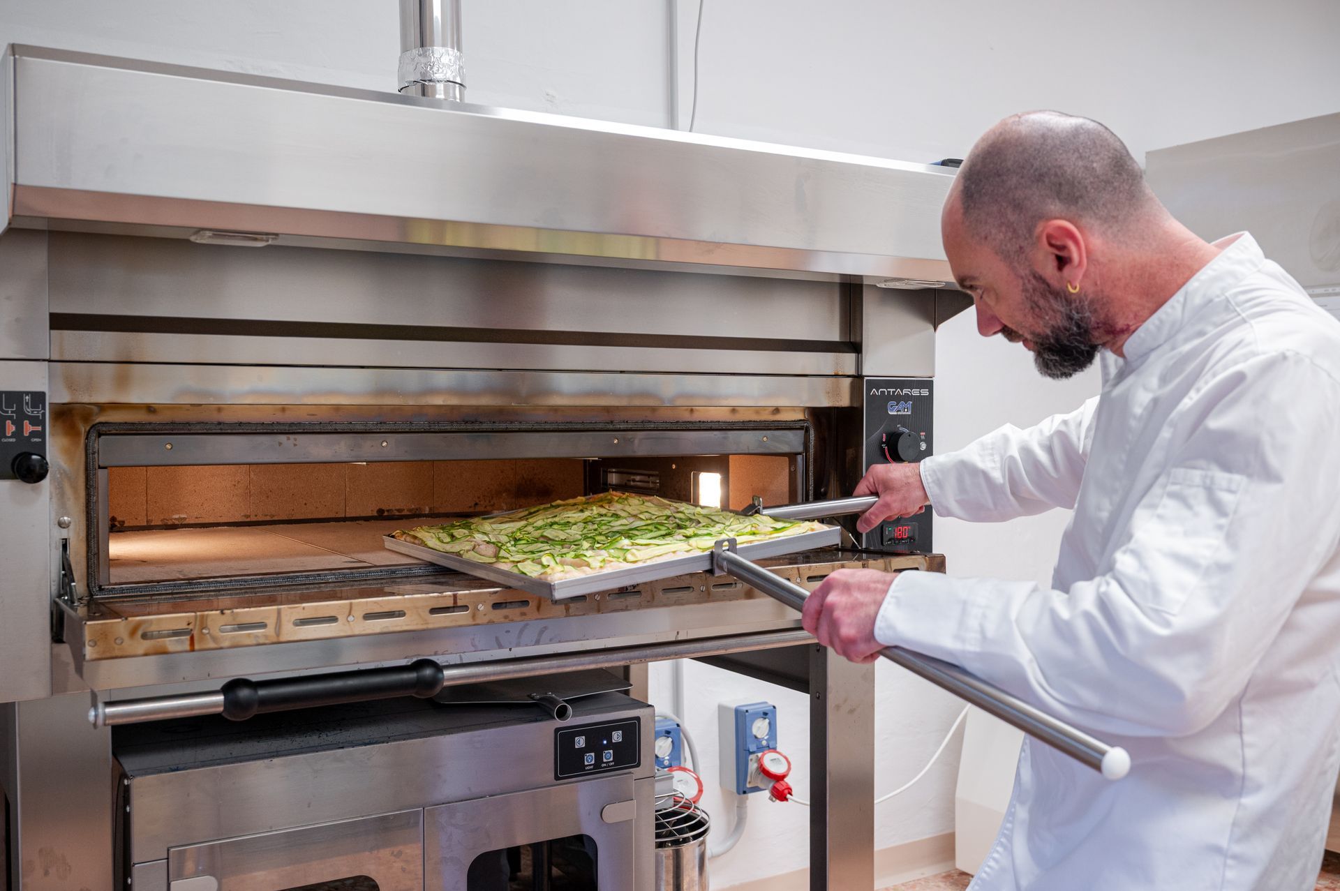 Lo chef inforna la pizza in un forno a legna usando una lunga pala di metallo.