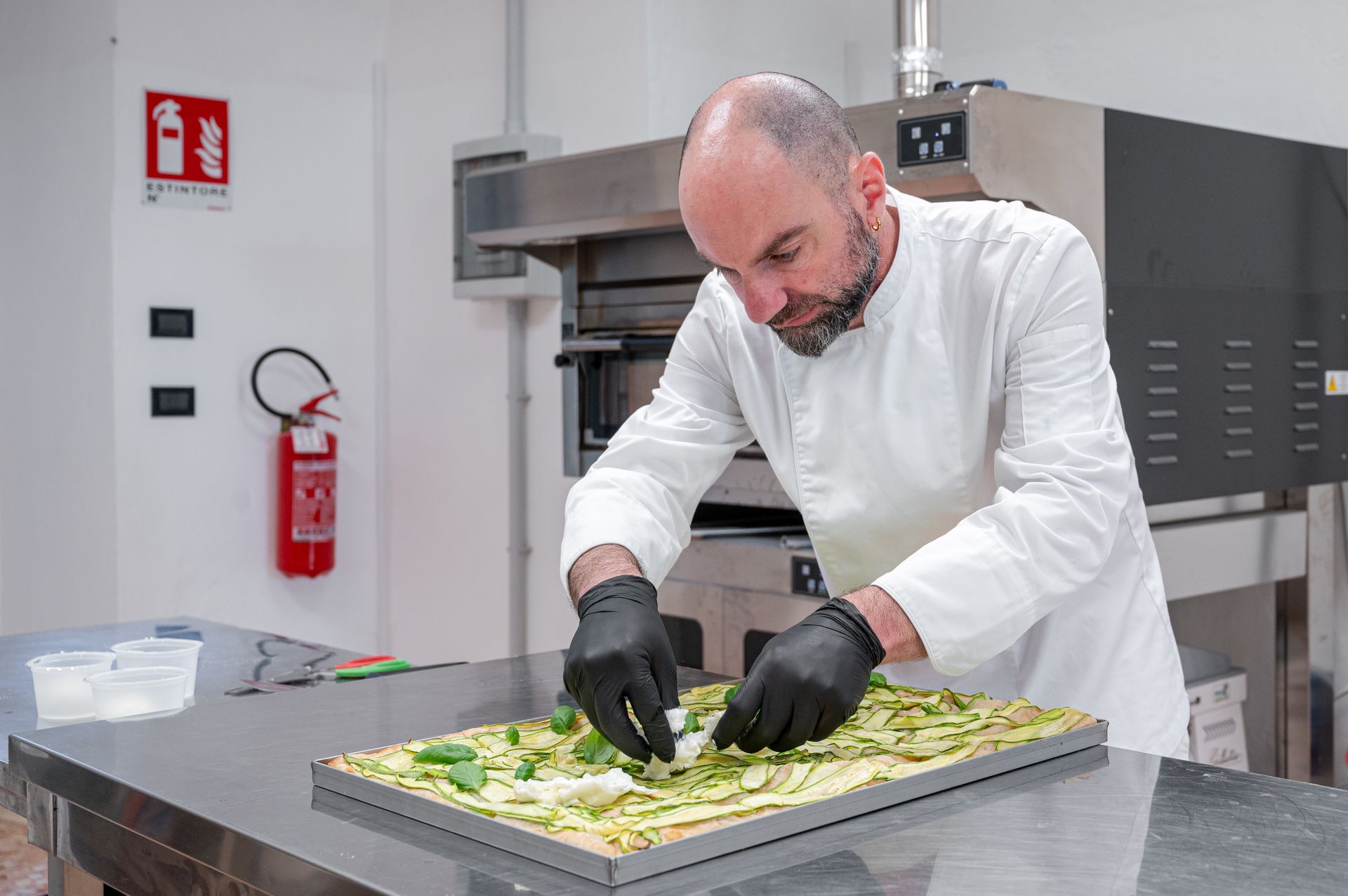 In una cucina professionale, uno chef in camice bianco sistema le verdure su un vassoio.