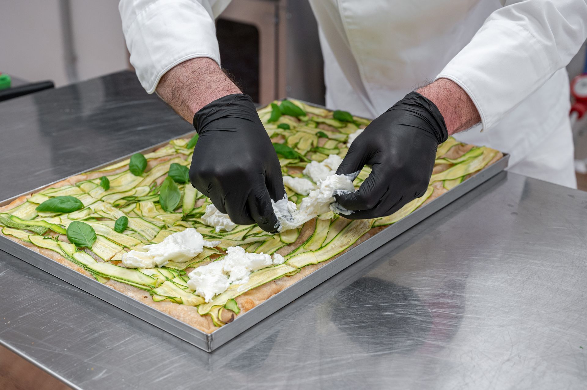 Uno chef sistema gli ingredienti per la focaccia su una teglia in cucina.