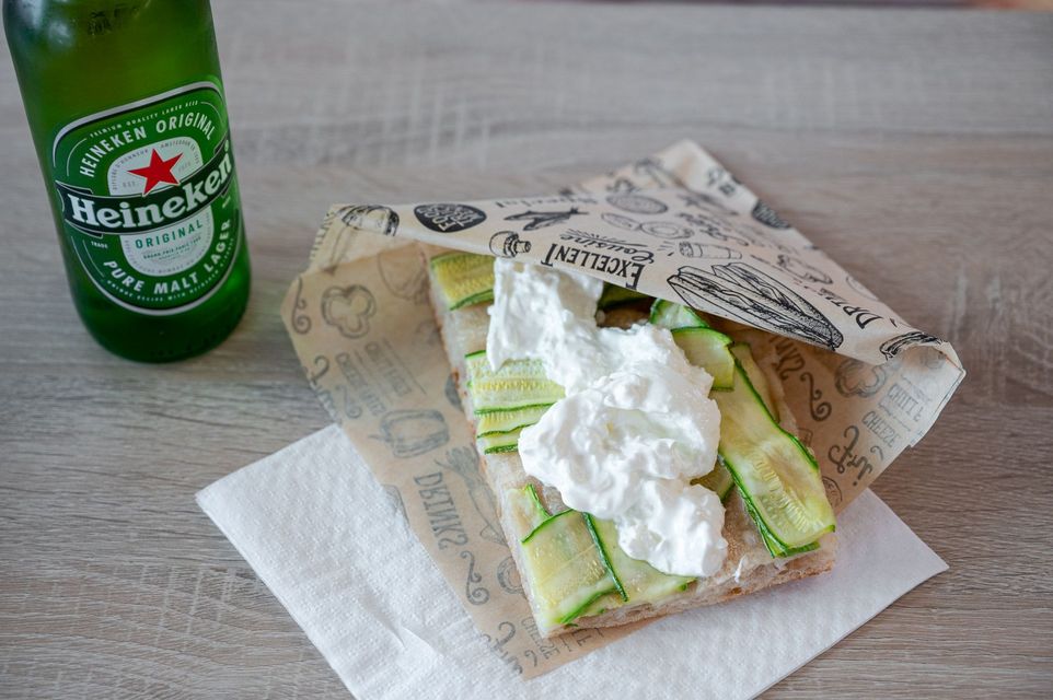Una bottiglia di birra Heineken accanto a un wrap con lattuga su un tovagliolo, guarnito con una salsa simile alla panna montata.