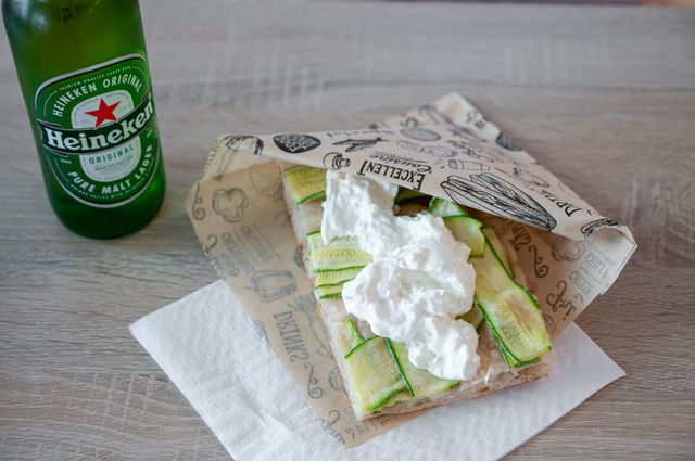 Una bottiglia di birra Heineken accanto a un panino aperto con lattuga e condimento cremoso su un tavolo.