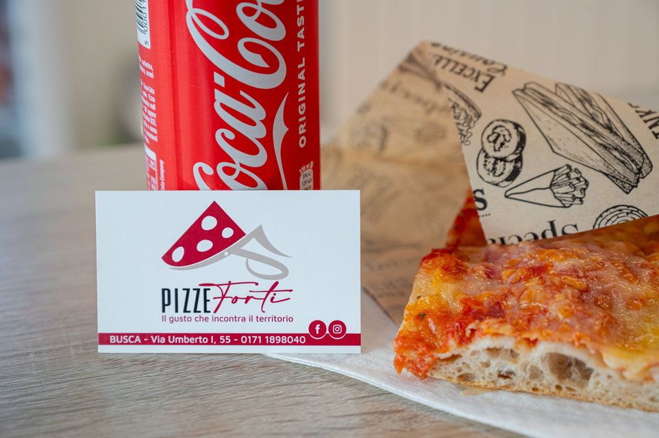 Una fetta di pizza con una lattina di Coca-Cola e una scatola di pizza di marca su un tavolo