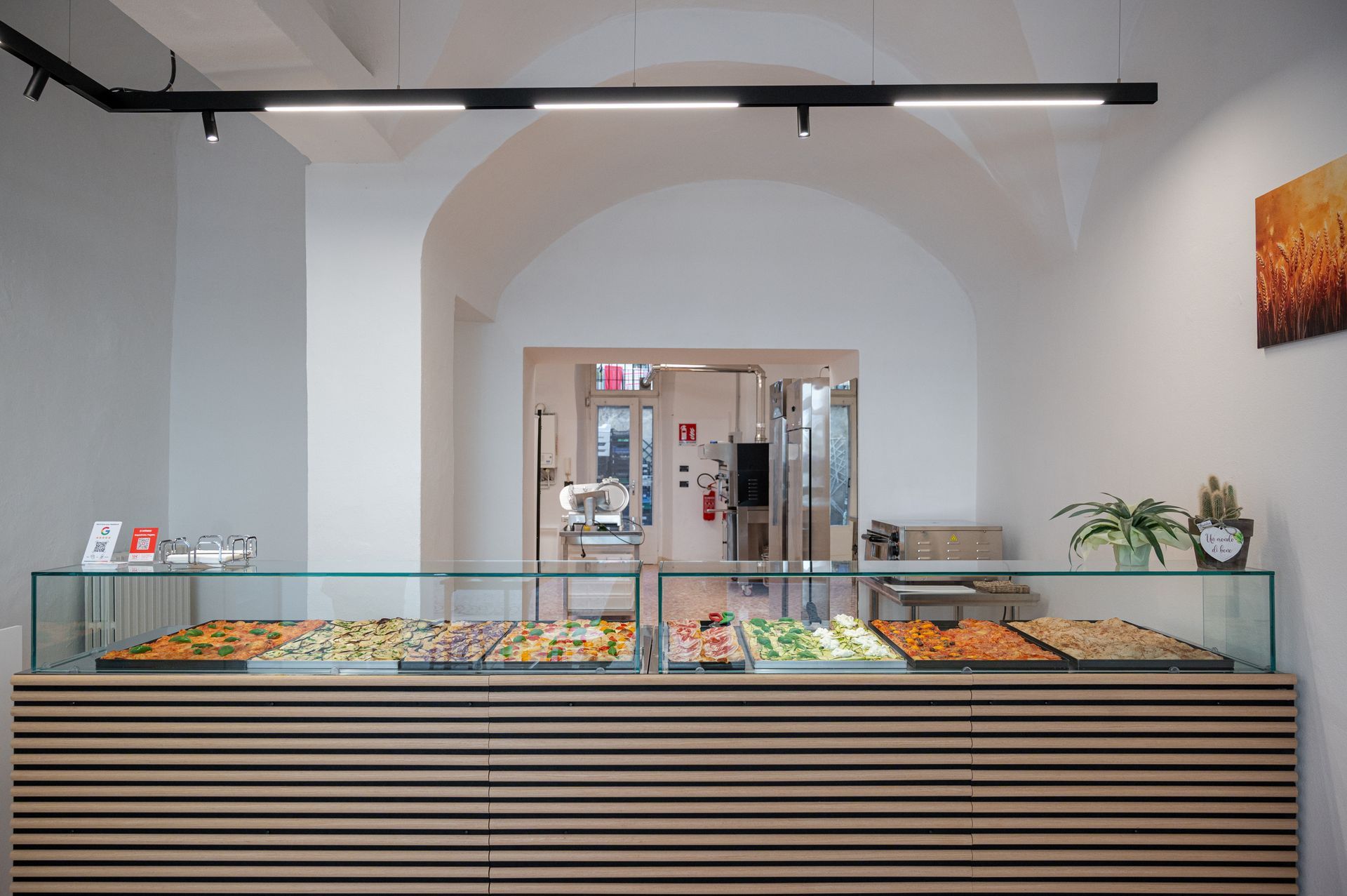 Bancone da bar moderno e minimalista con vetrina per dolci, listelli di legno e interno ad arco bianco.