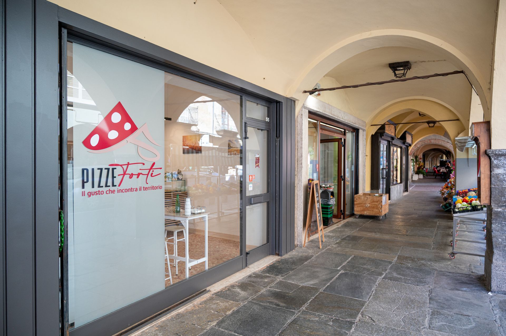 Portico coperto con negozi, tra cui una pizzeria sulla sinistra, e soffitti a volta.
