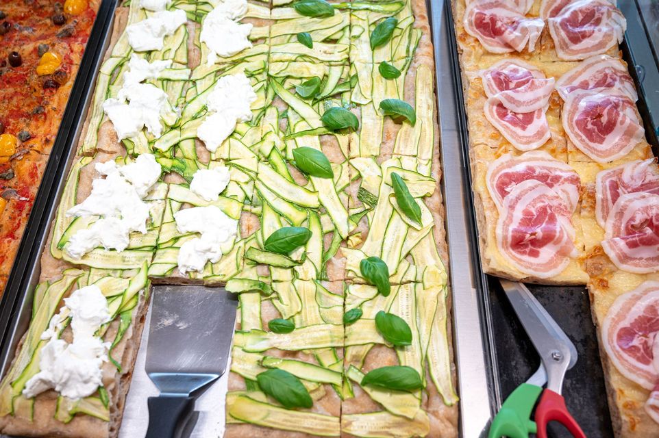 Vassoi di fette di pizza vegetariana e al salame piccante su un bancone, con pinze per servire le pizze.