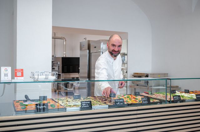 Un uomo dietro una vetrina di una pasticceria luminosa, sistema dei pasticcini colorati.