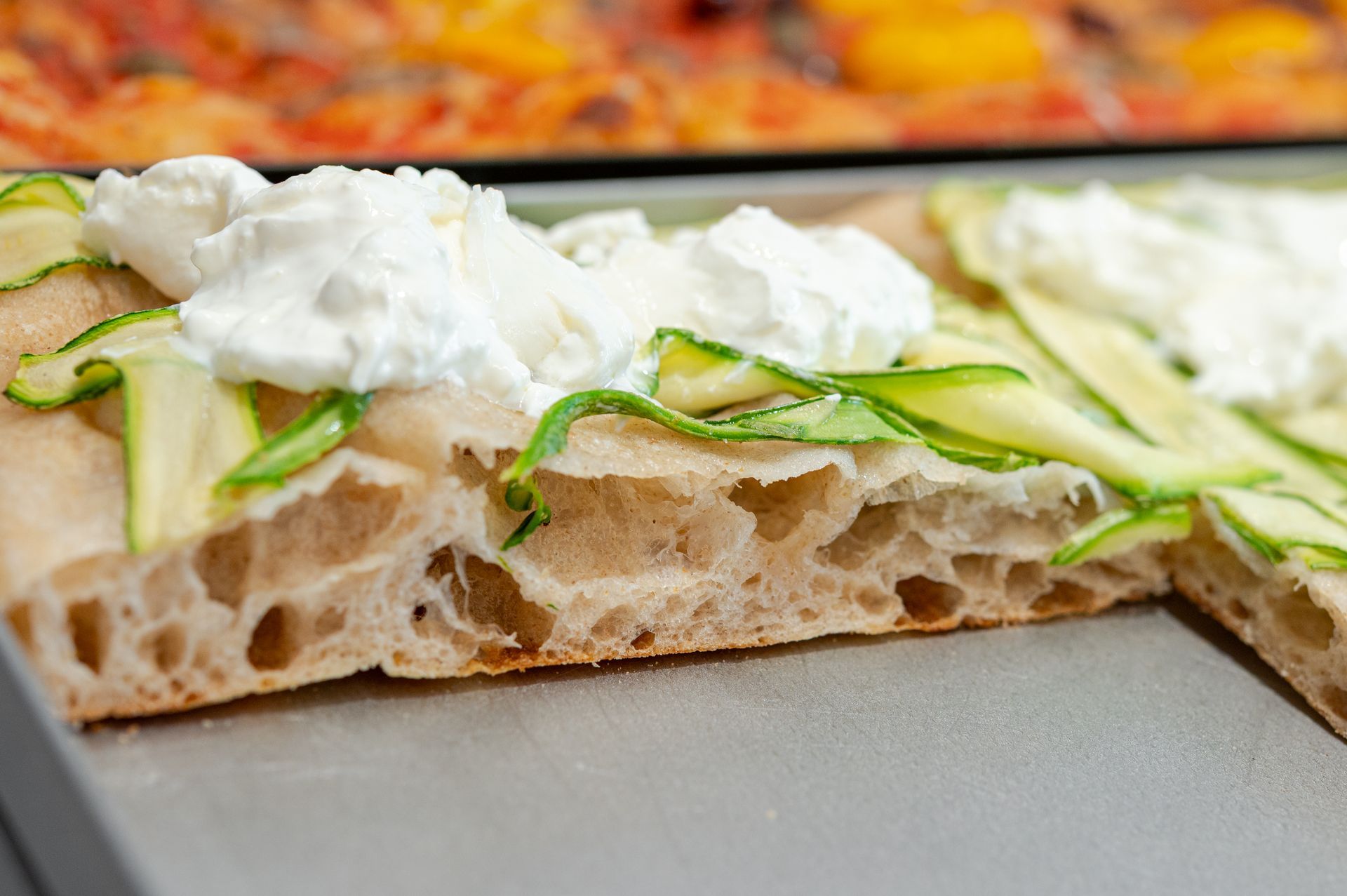 Primo piano di una focaccia guarnita con striscioline di zucchine e ciuffi di ricotta.