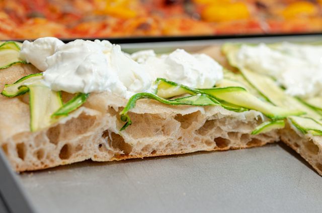 Primo piano di una focaccia guarnita con striscioline di zucchine e ciuffi di ricotta.
