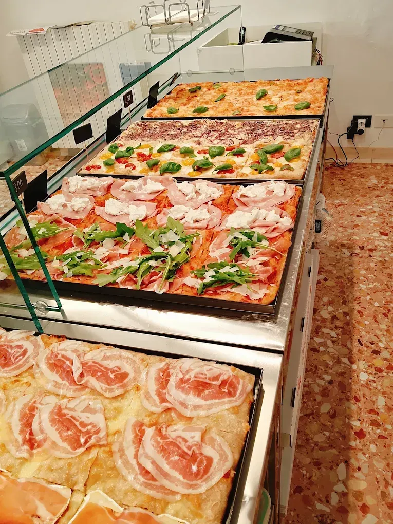 Vetrina da forno con un assortimento di pizze rettangolari condite con verdure, formaggio e affettati.