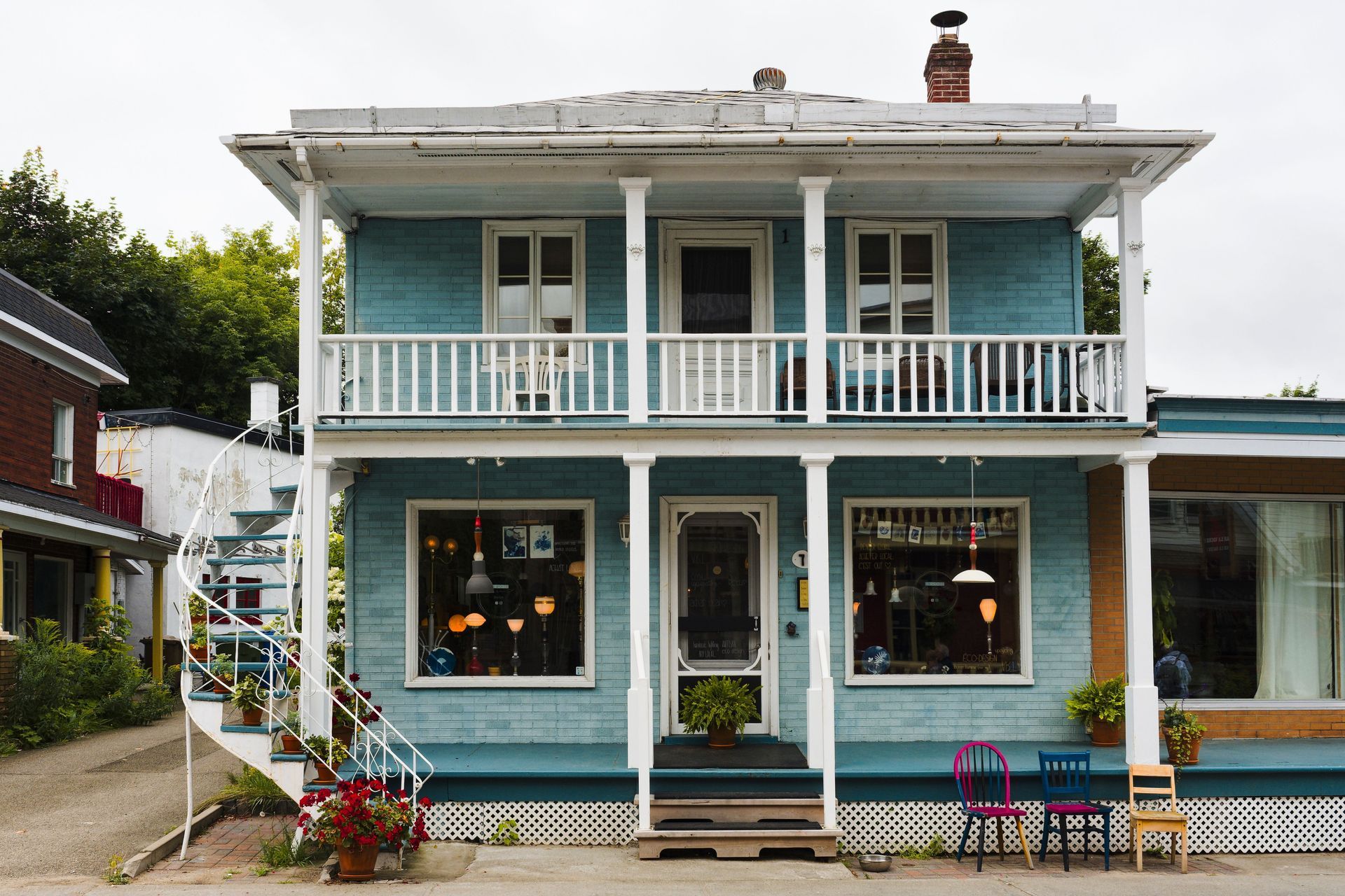 Boutique bleue à deux étages, avec des boiseries blanches, un balcon et des jardinières, à l’angle d’une rue