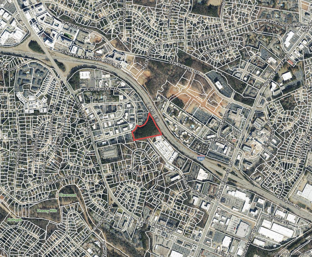 Aerial view of a town, with a red-outlined area on a green space bordering a highway and roads.