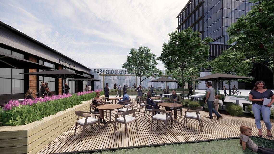 Outdoor dining area with tables, chairs, people, and buildings in the background. Greenery and a wood deck are present.