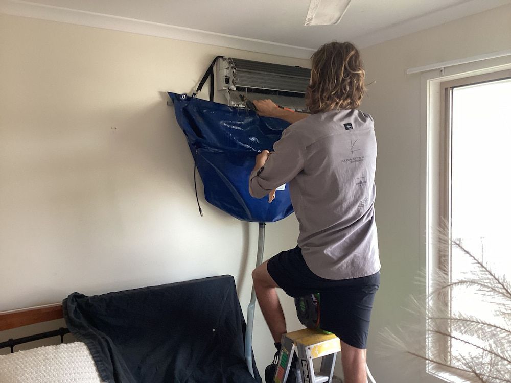 A Man is Cleaning an Air Conditioner in a Living Room — Kilowatts & Cool Whitsundays In Airlie Beach, QLD