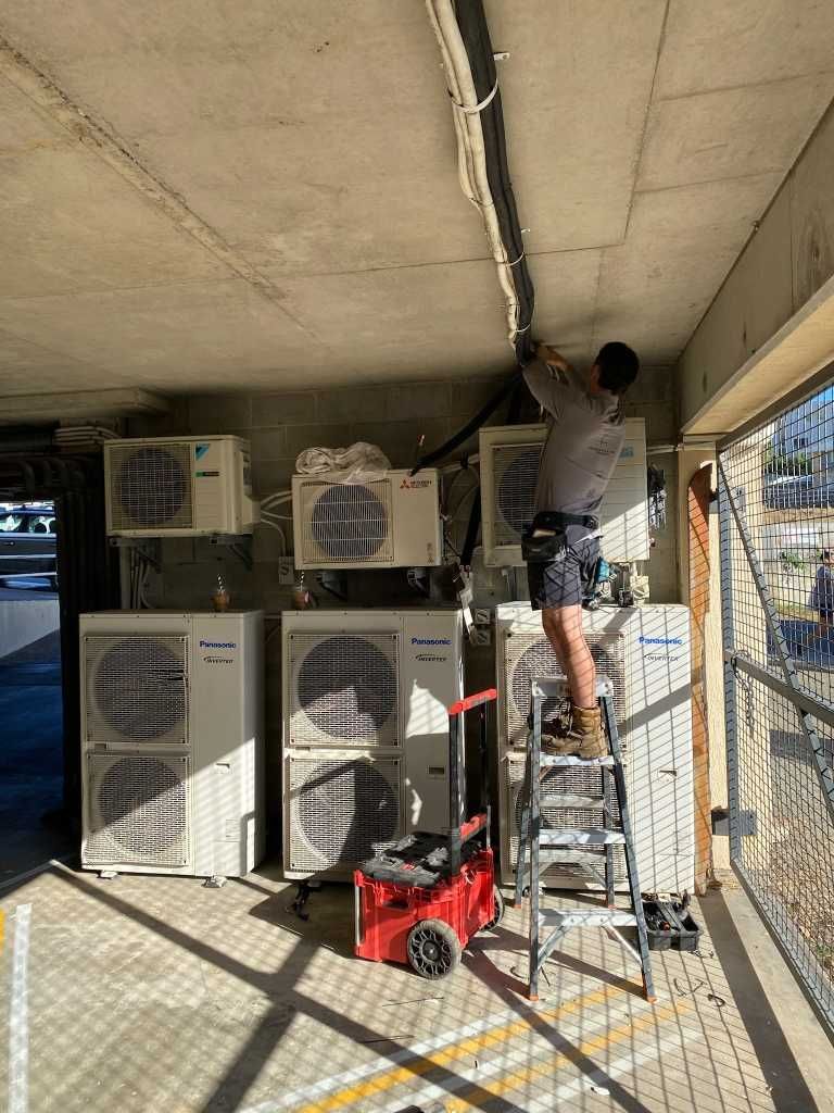 A Man is Standing on a Ladder Working on a Ceiling — Kilowatts & Cool Whitsundays In Strathdickie, QLD