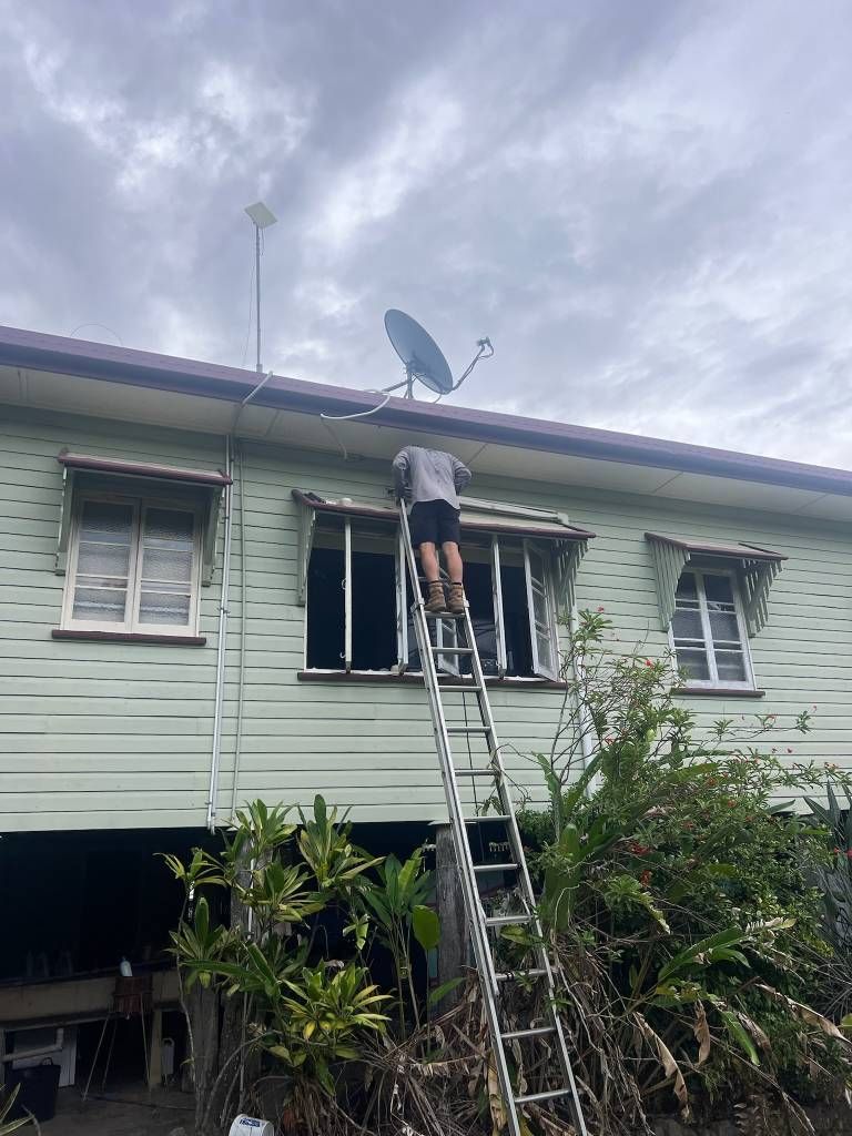 A Man is Standing on a Ladder in Front of a House — Kilowatts & Cool Whitsundays In Airlie Beach, QLD