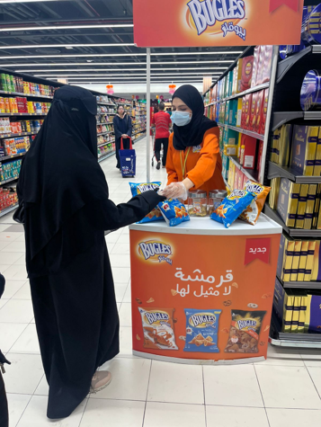 A woman wearing a mask is selling bugles chips in a store