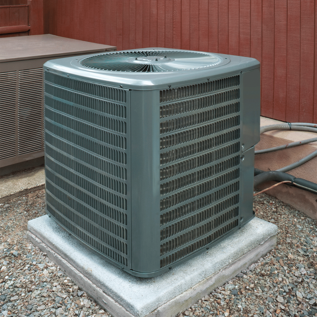 A large air conditioner is sitting on top of a pile of gravel.
