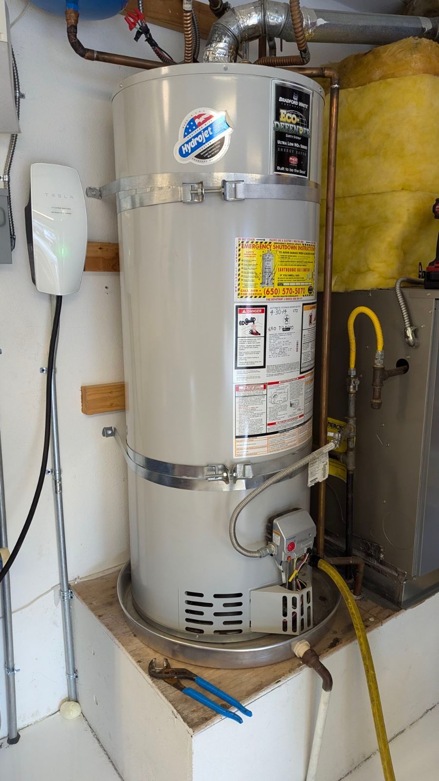 Two white water heaters with copper pipes and yellow gas lines in a utility room
