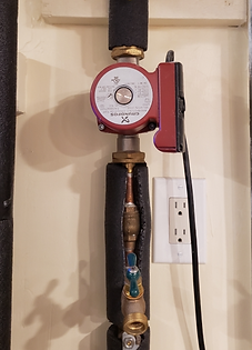Red circulator pump on insulated copper pipes beside a wall outlet in a utility room