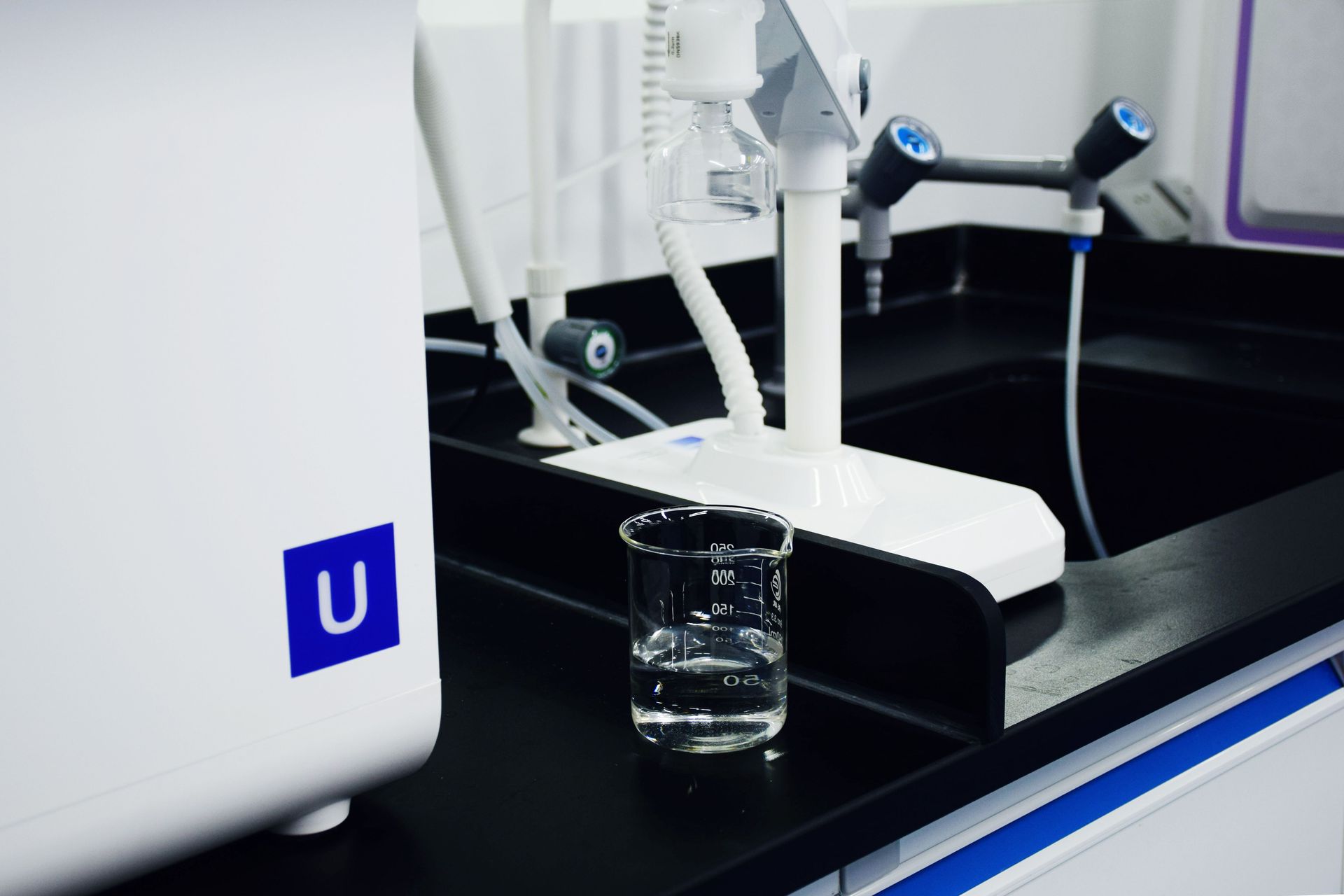 Lab robot arm dispensing liquid into a glass beaker on a black countertop