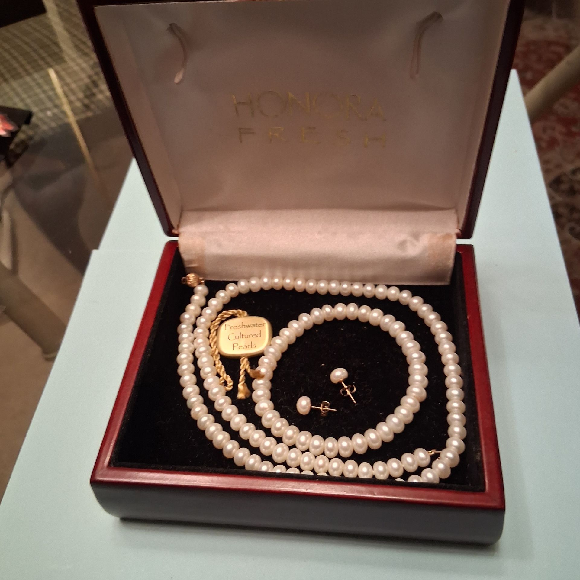 Pearl necklace and matching earrings in a red jewelry box with a gold seal and clasp