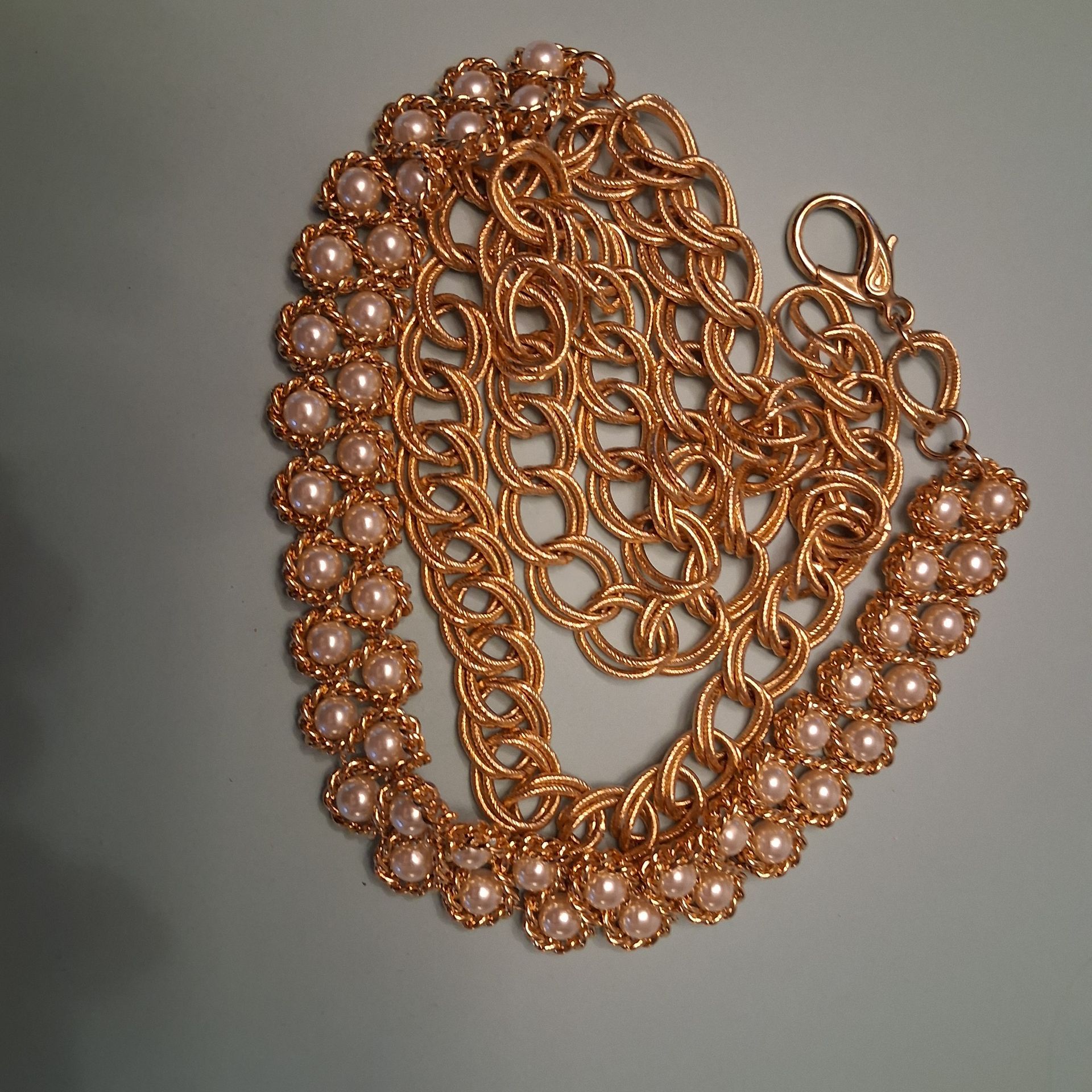 Rose-gold chain necklace with pearl-like bead accents on a gray background